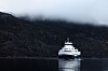 Hvit ferge på rolig fjord med tåkelagte fjell i bakgrunnen