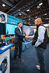 To menn håndhilser foran Odda Plast AS-stand på industrimesse.