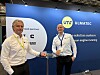 To menn står foran en blå Ulmatec-vegg og holder små glass i en presentasjonssituasjon.