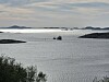 En liten båt ligger på åpent vann mellom lave øyer under en lys himmel.