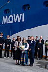 Blått Mowi-skip ved kai med en gruppe ansatte som står foran og holder blomster.