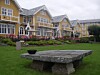 Gulmalte bygninger ved Solstrand Hotell omkranser en grønn plen med blomsterbed og en steinbenk.