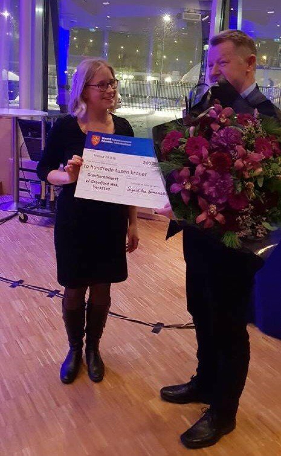 Her får daglig leder i GMV, Bård Meek-Hansen overlevert blomster og sjekken på to hundre tusen kroner av fylkesråd for kultur og næring i Tromsø, Sigrid Ina Simonsen. Foto: GMV.
