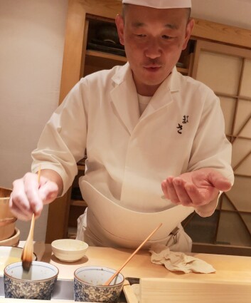 Sushi-chef Masakatsu Oka  gir et lite penselstrøk som siste finish på fisken før han overleverer en av de over seksti bitene. Foto: Ole Andreas Drønen.