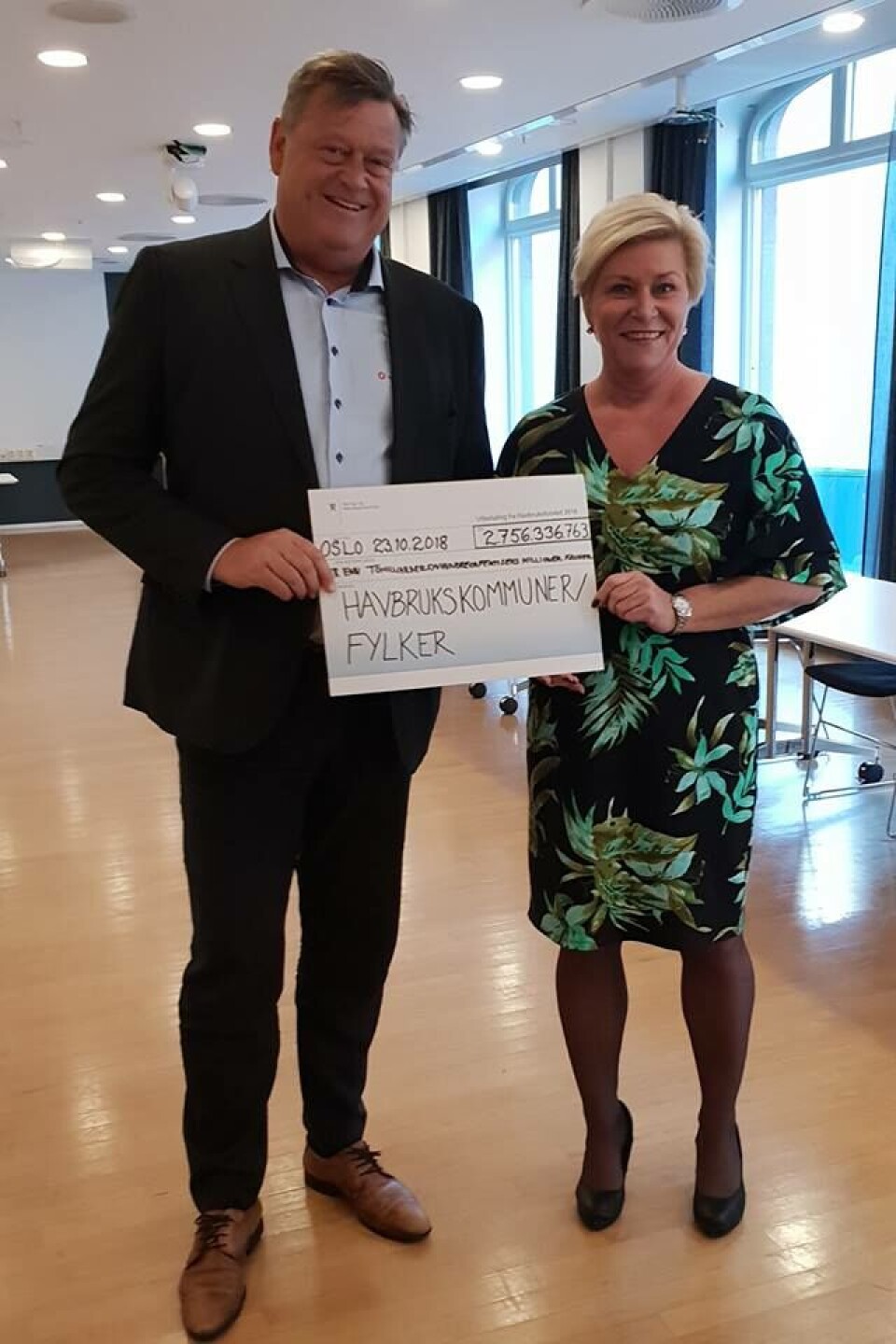 Fiskeriminister Harald Tom Nesvik og finansminister Siv Jensen her med sjekken på over 2, 75 milliarder kroner fra havbruksfondet som går til oppdrettskommunene i landet. Foto: Facebook/Harald Tom Nesvik.
